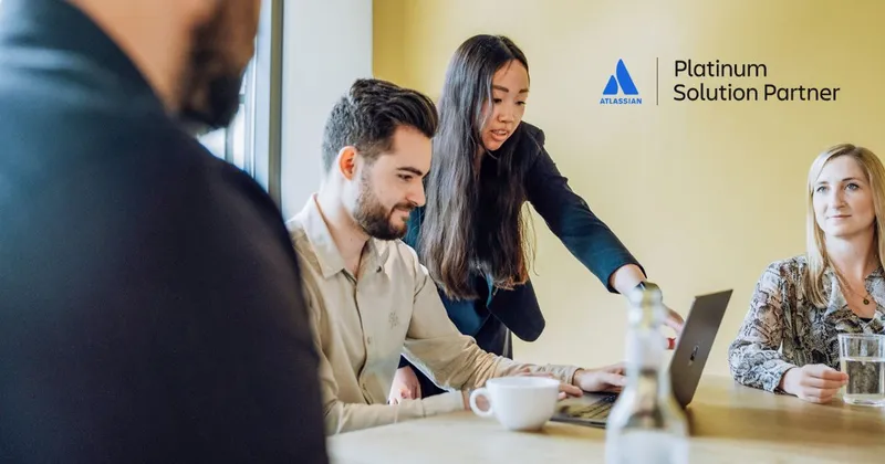 Two women and a man in an office setting, with one woman pointing at a laptop screen while others observe. The Atlassian Platinum Solution Partner logo is in the upper right corner.